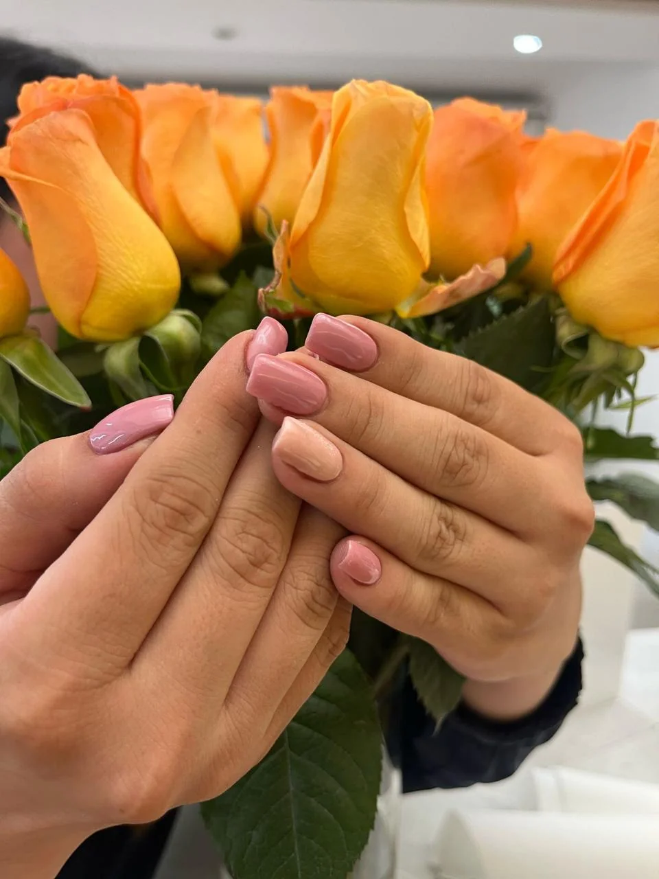 Manicure rosado frente a flores amarillas en Aura Nails Care